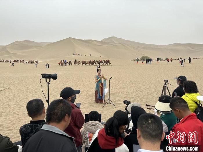 圖為2023年4月底，敦煌大漠“逐舞者”奧楠在鳴沙山月牙泉景區(qū)視頻直播，吸引游人圍觀。　馮志軍 攝